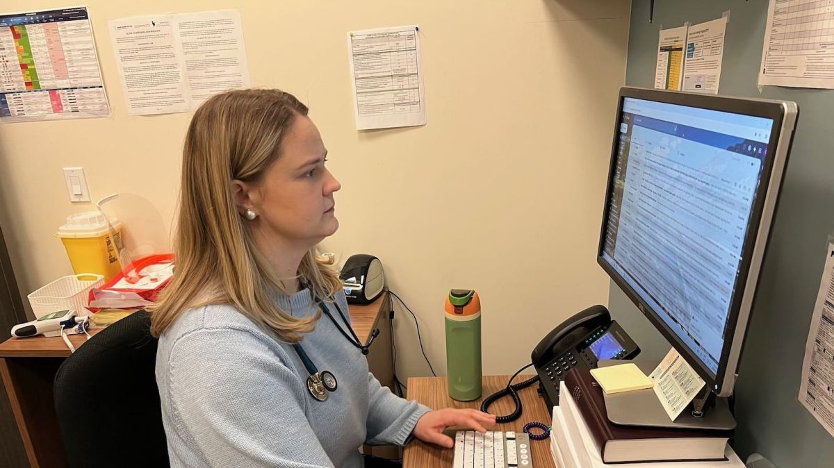 Семейный врач в Канаде работает за компьютером с медицинскими документами.