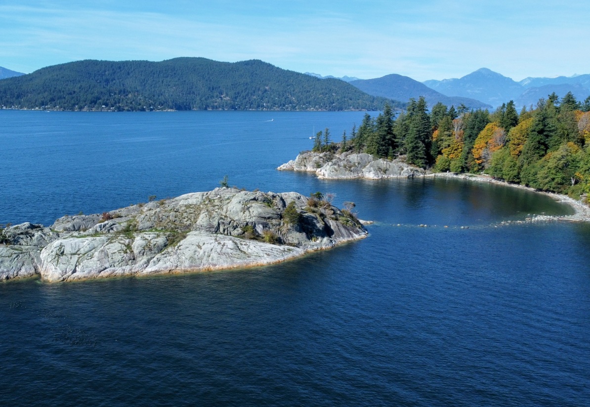 дайвер погиб ванкувер | Наш Ванкувер Rocky shoreline extending into a calm blue lake, with evergreen trees on a forested peninsula and distant mountains.