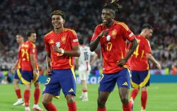 Spain national team players celebrate on the pitch, wearing red shirts with yellow trim and blue shorts.