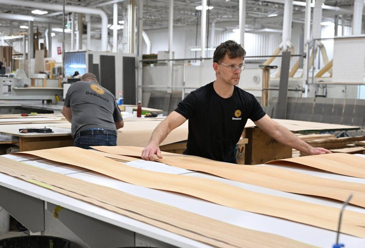 канада древисиеа | Наш Ванкувер Two workers in a large workshop lay out long curved wooden panels on a worktable, focused on their task while wearing protective gear.