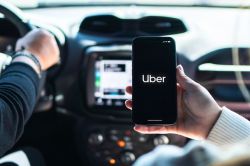 Экран смартфона с приложением Uber и уведомлением об оформлении подписки Uber One на фоне города в Канаде