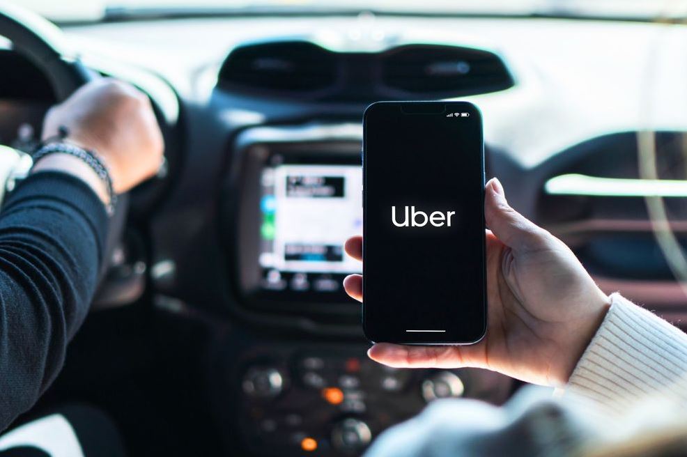 Коллективный иск против Uber Экран смартфона с приложением Uber и уведомлением об оформлении подписки Uber One на фоне города в Канаде