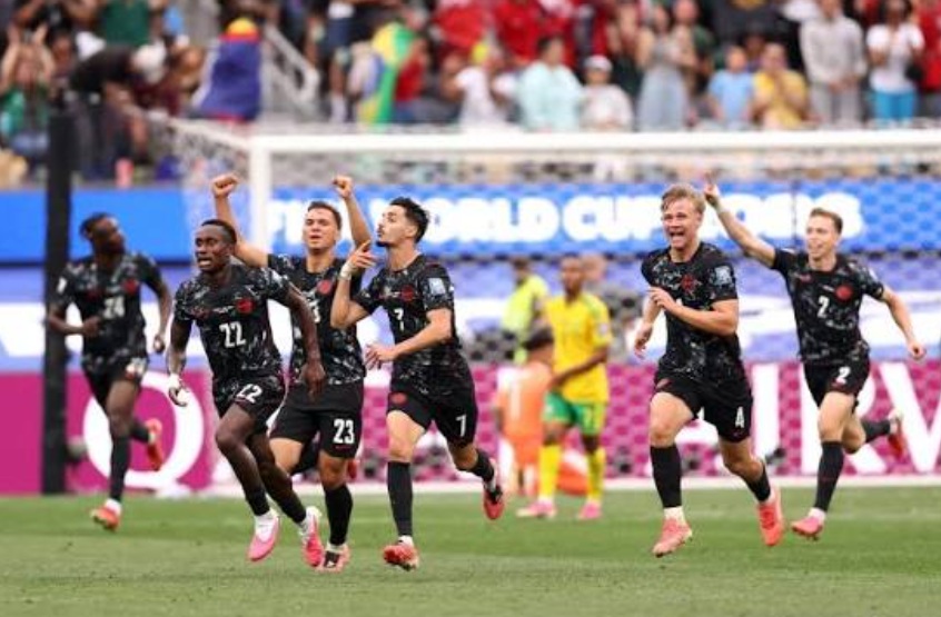 A soccer team in black uniforms celebrates a goal, running across the field as fans cheer in the stands.