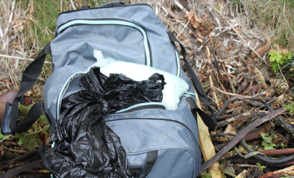 НАркотики граница сша | Наш Ванкувер Blue backpack on the ground with black and white garbage bags sticking out, in a grassy, outdoor area with leaves and debris nearby.