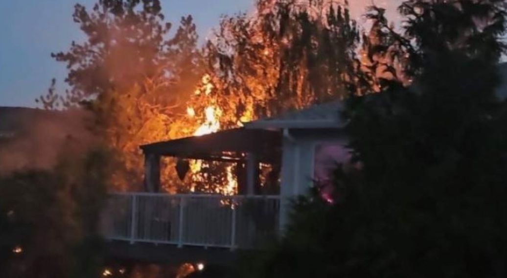 поджоги в келоуне | Наш Ванкувер Deck or balcony of a house engulfed in flames with trees in the background at dusk/early evening.