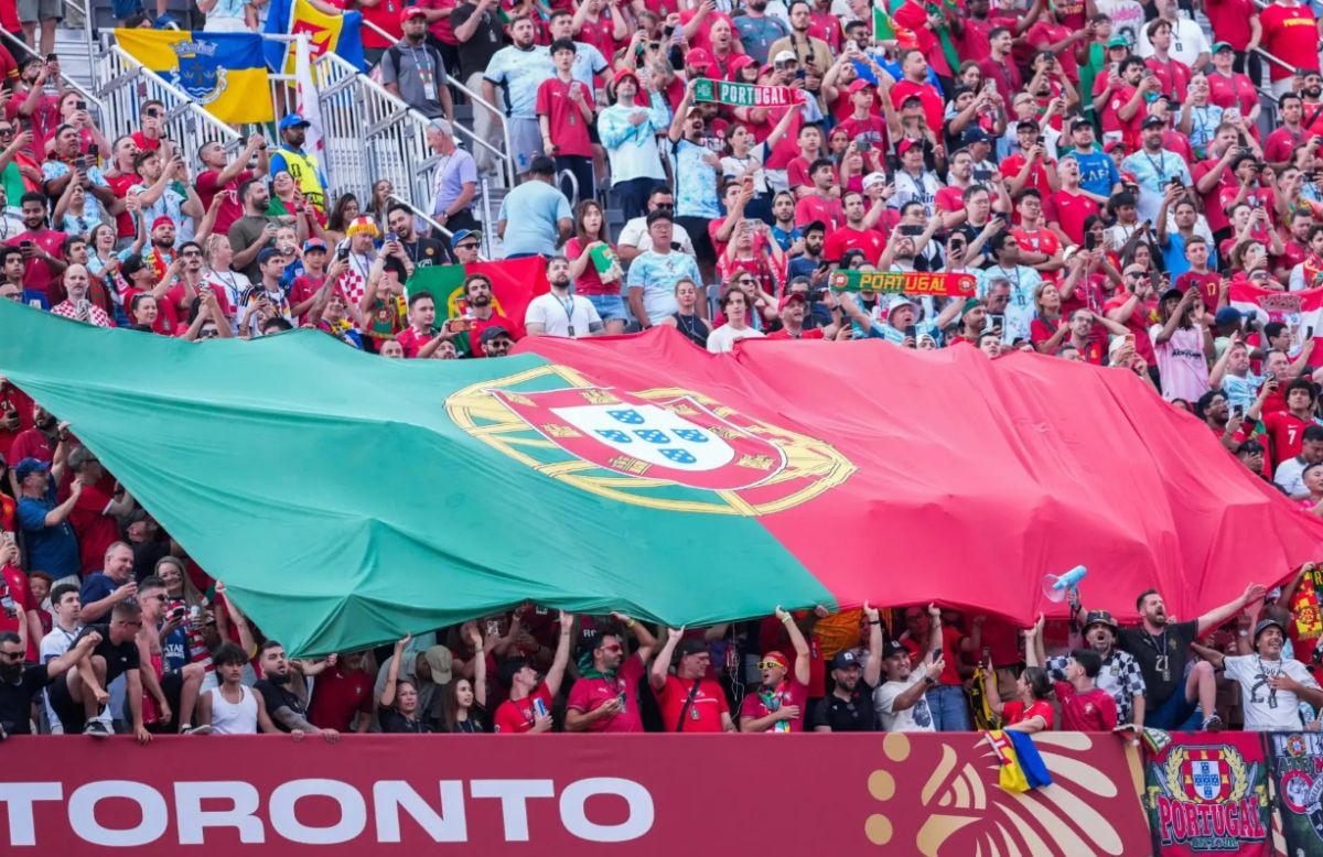 Crowd of soccer fans waving a large green‑red Portugal flag across the stands.