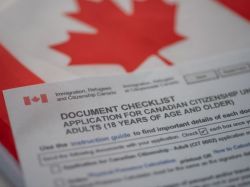 Close-up of a Canadian flag with a printed immigration document titled 'Document Checklist: Application for Canadian Citizenship (Adults 18 years and older)'.