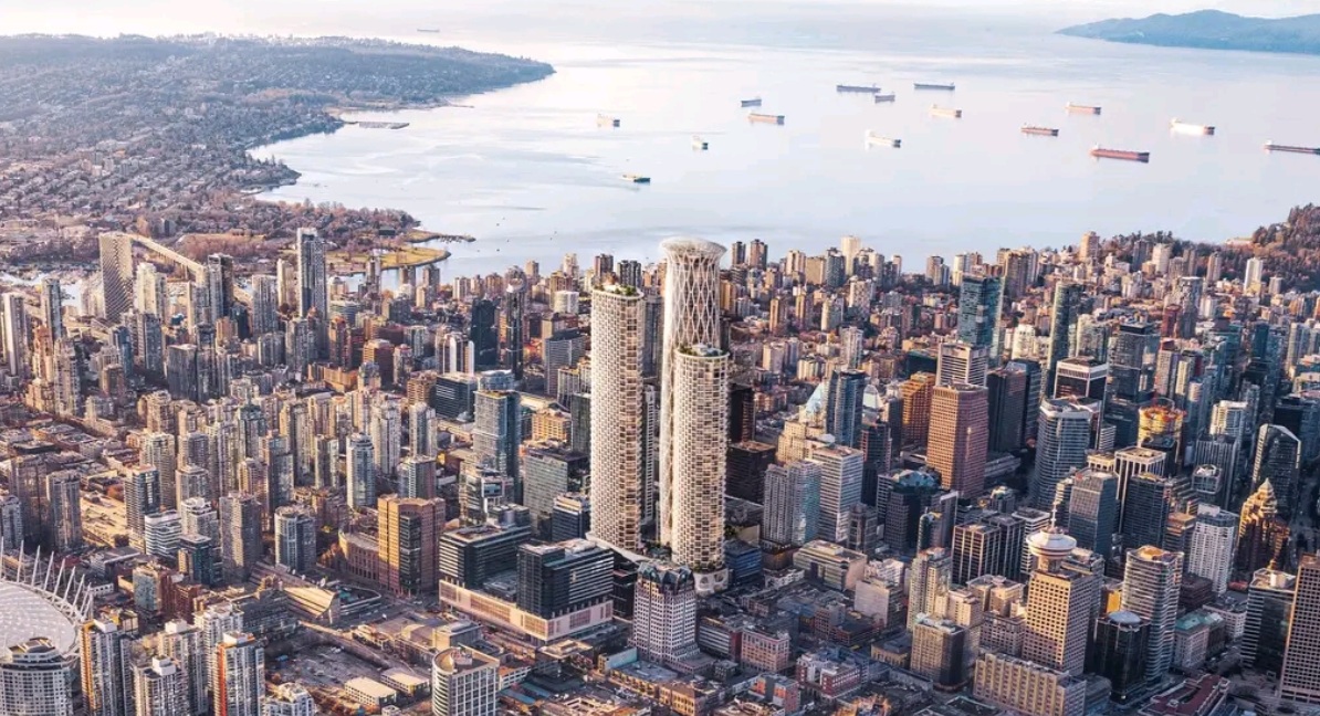A dense city skyline with two tall modern towers and a harbor with numerous ships beyond the buildings, viewed from above.