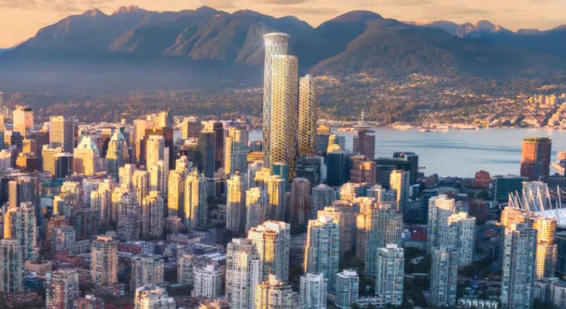 Aerial view of a densely built city skyline at sunset with tall skyscrapers and mountains in the distance.