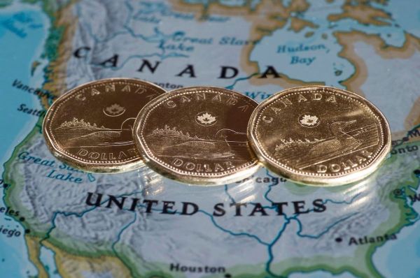 Three Canadian dollar coins lying on a map showing Canada and the United States.
