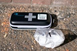 Naloxone overdose kit in a black case with a white cross on a rough pavement surface.