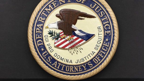 Seal of the U.S. Department of Justice featuring an eagle over a patriotic shield and motto, set on a dark background