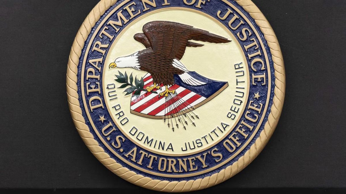 Seal of the U.S. Department of Justice featuring an eagle over a patriotic shield and motto, set on a dark background