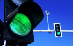 Close-up of a green traffic light with a second green signal in the background against a clear blue sky.