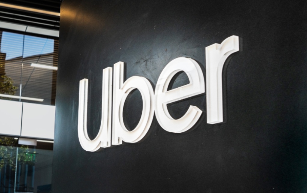 убер | Наш Ванкувер White Uber logo mounted on a dark wall outside a modern office building.