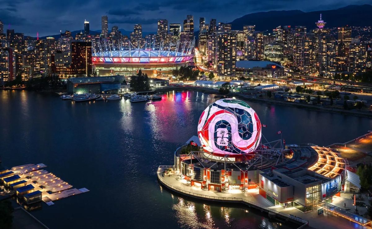 Nighttime city skyline over a harbor with a giant illuminated soccer ball sculpture by the waterfront stadium?