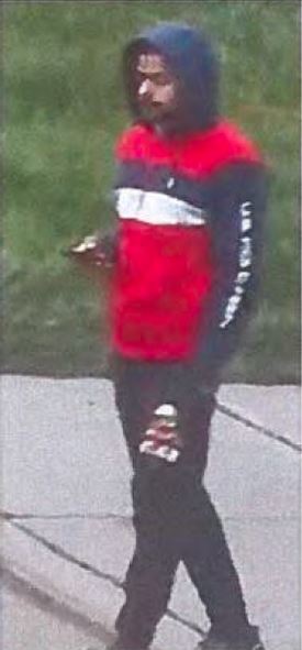 Анмол Бишной | Наш Ванкувер Person wearing a red and black hoodie with a white stripe across the chest, hood up, walking on a sidewalk and looking down at something in their hand.