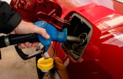 Person refueling a red car with a blue gas nozzle at a gas pump.