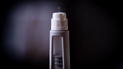 Close-up of a white medical injection pen with the needle exposed against a dark background.