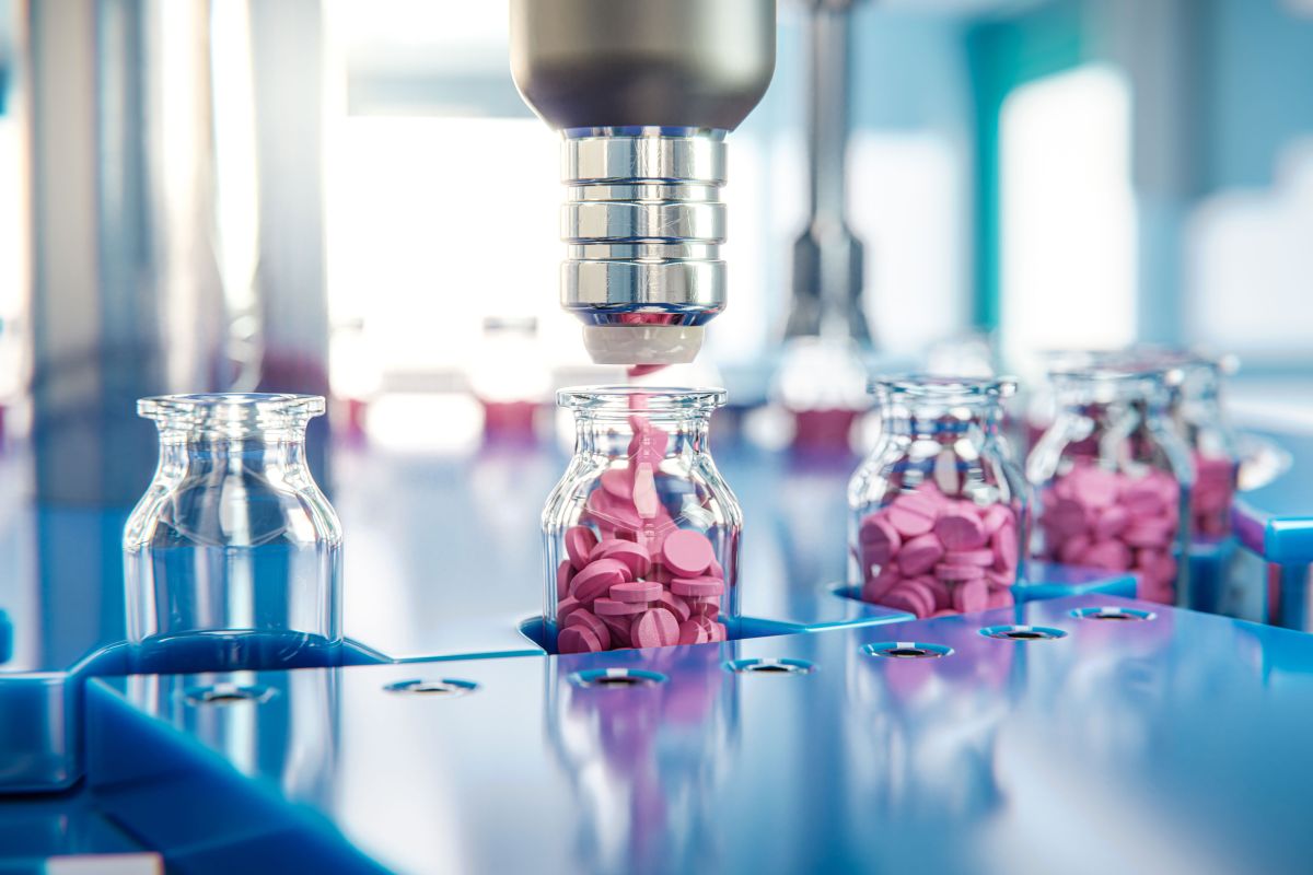 Фармацевтические компании | Наш Ванкувер Automated pill-filling line placing pink tablets into glass vials on a blue conveyor.