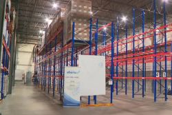 Warehouse with tall blue-and-red pallet racks, pallets stacked on top shelves, wide aisle, and a Featured Alberta banner in front.