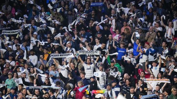 Crowd of Vancouver Whitecaps FC supporters in the stands, many waving white and blue scarves at a match.
