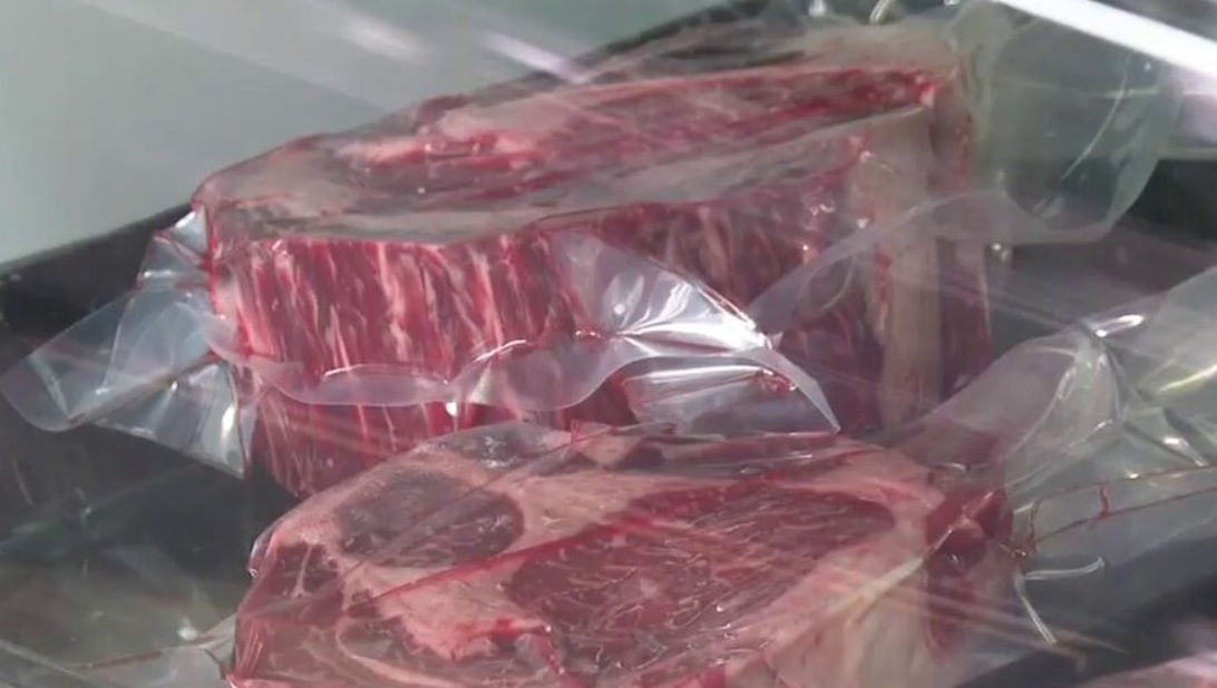Two uncooked beef ribeye steaks vacuum-sealed in clear plastic, resting on a reflective surface.