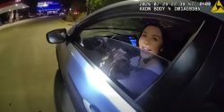 Woman in a car at night, smiling at the camera from the driver's seat, with a timestamp overlay and streetlights in the background.