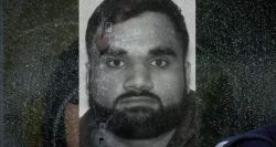 Grayscale portrait of a man with short hair and full beard looking straight at the camera, with a cracked/ distressed overlay across the image.