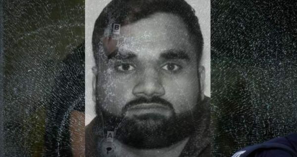Grayscale portrait of a man with short hair and full beard looking straight at the camera, with a cracked/ distressed overlay across the image.