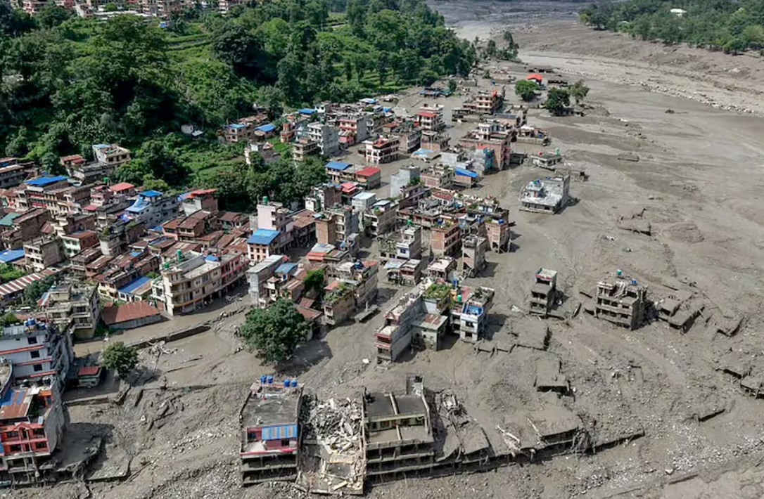 канада помощь непалу | Наш Ванкувер A densely built hillside town on a muddy riverbank with many damaged and collapsed buildings amid debris after a disaster.