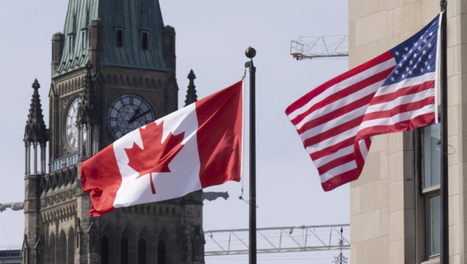Canadian flag and United States flag waving on flagpoles in front of a historic clock tower building in Ottawa (Peace Tower).