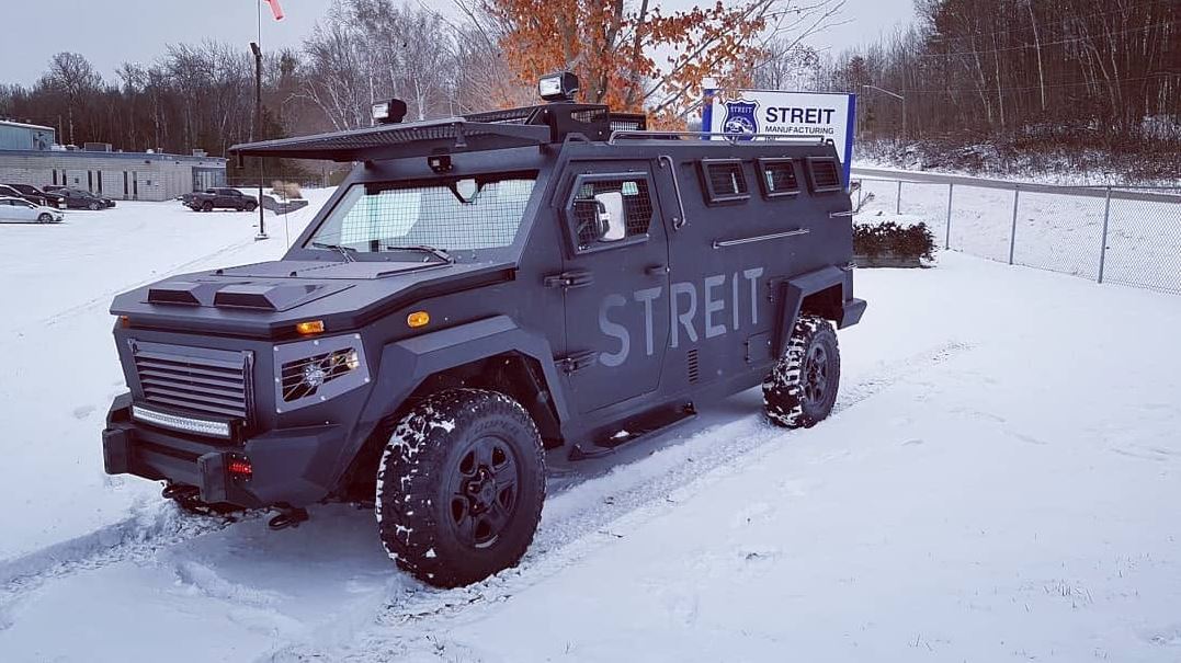 Armored vehicle with 'STREIT' branding parked in a snowy lot, rugged tires and roof equipment visible.