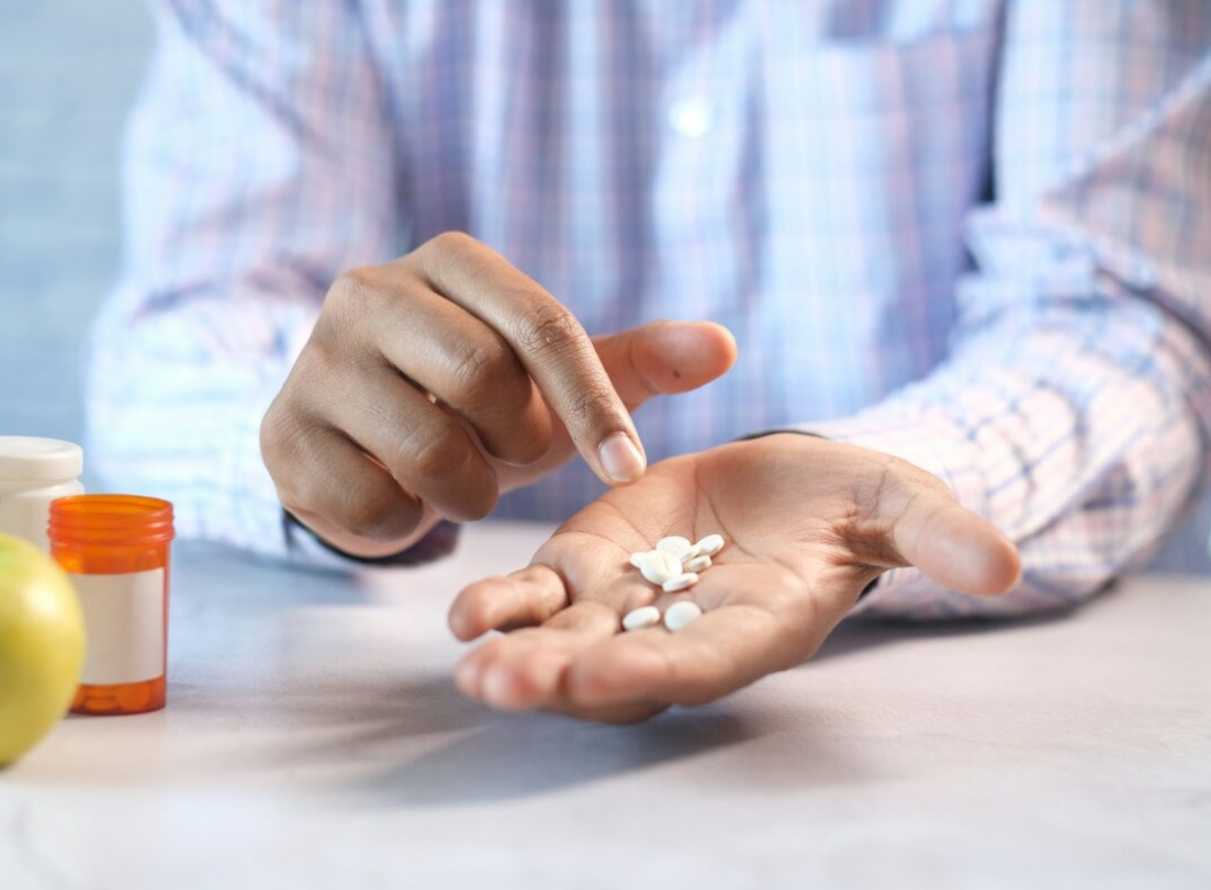 Open palm showing white tablets; prescription bottles on the table nearby