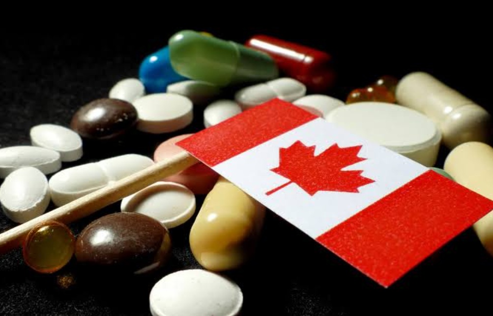 Canadian flag placed on a toothpick among assorted pills and capsules on a dark background, conveying a medical/drug theme