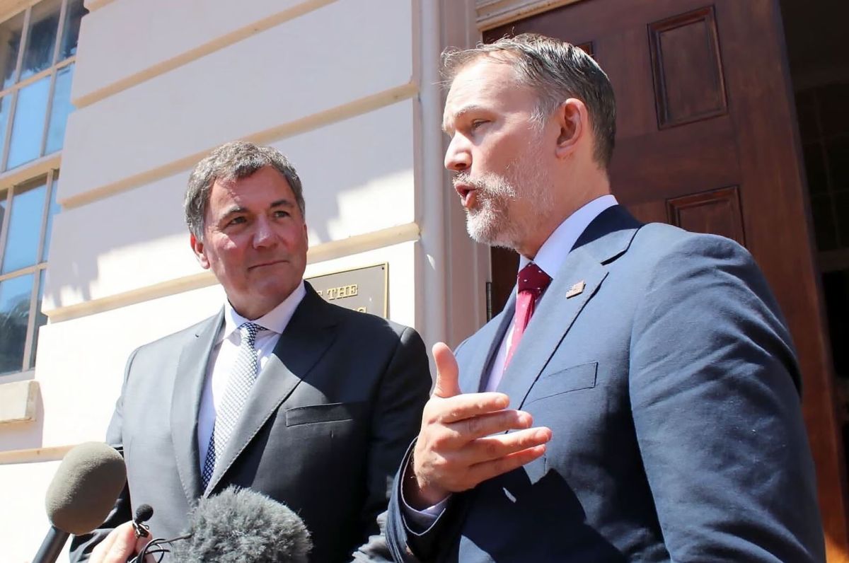 Министр торговли Канады | Наш Ванкувер Two men in suits speak to reporters outside a building, with microphones in the foreground; one man gestures as he talks while the other listens.