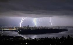 Nighttime city skyline illuminated by multiple bright lightning bolts over the water.