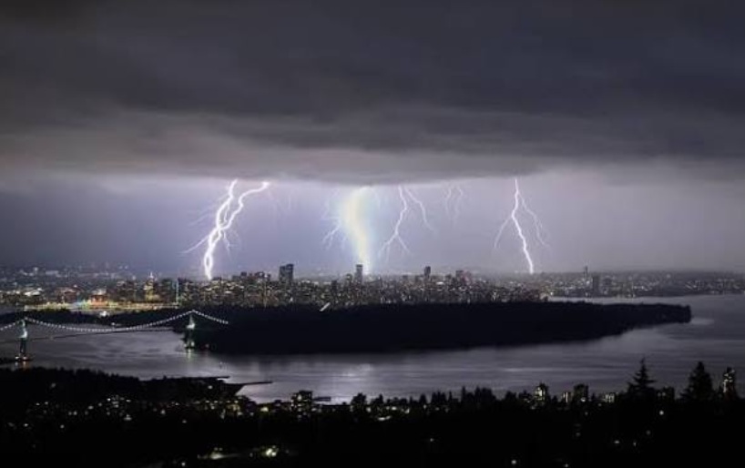 Nighttime city skyline illuminated by multiple bright lightning bolts over the water.