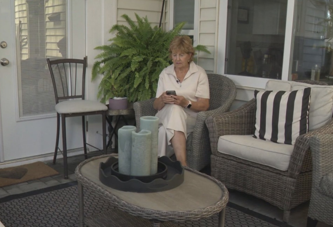 мошенничество телефоны | Наш Ванкувер Elderly woman on a wicker porch chair, looking at her smartphone, with a fern behind and candles on the table in front of her.