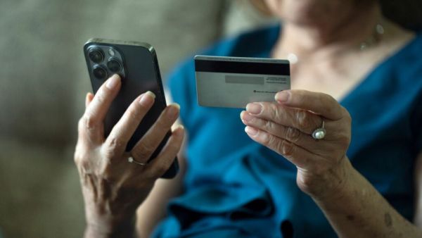 An older woman holds a smartphone in one hand and a credit card in the other, ready to pay online or in-store.
