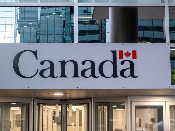Налоги канадцев | Наш Ванкувер Sign reading 'Canada' with a small Canadian flag above, at the entrance of a modern glass-fronted building.