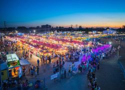 Busy night market with colorful stalls, string lights, and a crowd of shoppers at sunset festival.