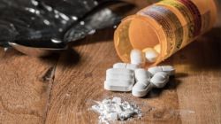 Prescription bottle tipped over, white tablets spilled onto a wooden surface with a small pile of powder nearby.