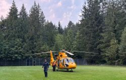 Orange rescue helicopter on a grassy field with crew members nearby and dense trees in the background.