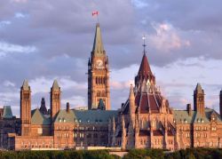 Ottawa's Parliament Hill skyline featuring the Peace Tower and Gothic Revival buildings under a dusky sky with a flag atop the tower