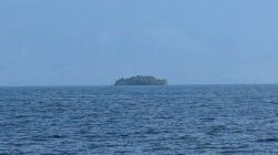 Distant tree-covered island on the horizon over a calm blue sea.