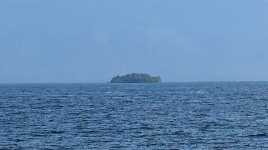 Distant tree-covered island on the horizon over a calm blue sea.