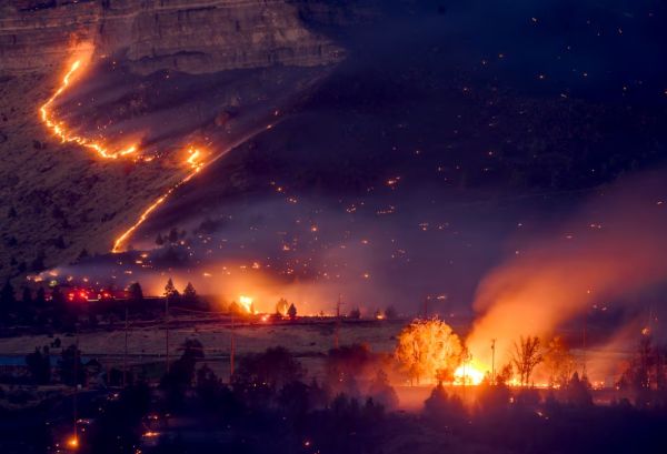 Nighttime hillside wildfire with flames following a ridge and spreading toward a town area