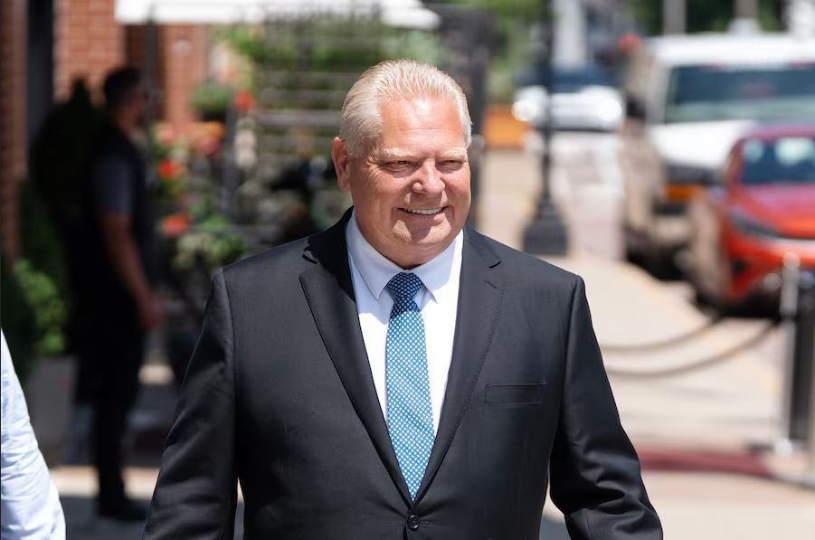 Smiling older man in a dark suit and blue tie walks outdoors on a sunny city street.
