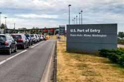 Cars line up at a U.S. port of entry near Peace Arch in Blaine, Washington, with a large entry sign on the right.